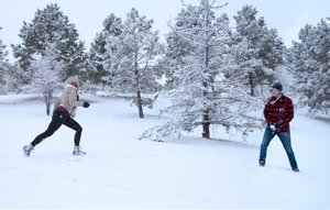 Ein junges Pärchen liefert sich im verschneiten Wald eine kleine Schneeballschlacht. Beide tragen Winterkleidung und Schneeschuhe von Xero Shoes.